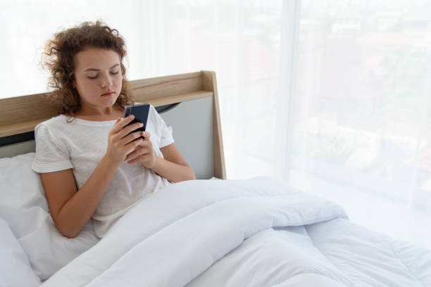 Junge schöne glückliche Frau, die sich entspannt und Smartphone benutzt, während sie morgens nach dem Aufwachen im Bett liegt. – Foto