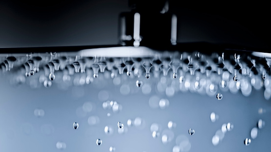 Close-up of water drop flowing from shower head in bathroom.