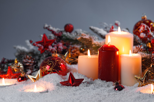 Christmas backgrounds: three red burning Christmas candles shot on rustic wooden table. The composition is at the left of an horizontal frame leaving useful copy space for text and/or logo at the right.\nString light and Christmas decoration are out of focus at background. Predominant colors are red and brown. High resolution 42Mp studio digital capture taken with Sony A7rII and Sony FE 90mm f2.8 macro G OSS lens