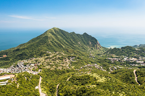 This breathtaking photograph captures a natural wonder in Taiwan, inviting viewers on an adventurous journey. In the foreground, the ancient town of Jiufen clings to the steep mountainside, with its distinctive architectural style and stone-paved alleyways adding character to the landscape. As the gaze extends into the distance, the majestic Keelung mountain range envelops the entire area, presenting a grand and awe-inspiring vista.\n\nWhat's truly astonishing is the sea, bathed in the golden hues of the setting sun, radiating a warm glow that seems like a precious gift from nature to this land. The Golden Sea stretches serenely towards the horizon, harmonizing with the azure sky to create a beautifully balanced scene.\n\nThis photograph is rich with narrative potential. Editors creating a travel guide can weave stories about the history of Jiufen town, the grandeur of the Keelung mountains, and the symbolism of the Golden Sea, immersing readers in an adventure filled with surprises and wonder, enticing them to delve deeper into this stunning landscape.