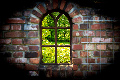 An old window in a brick wall with a green garden in the background