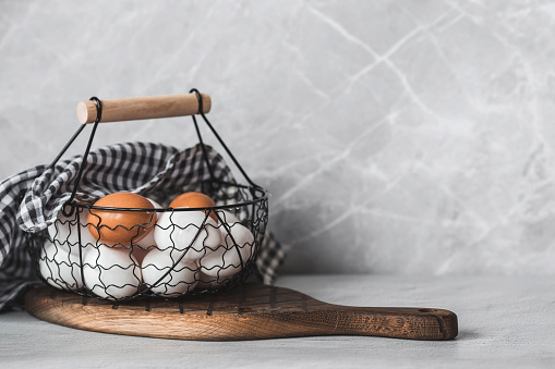 Fresh farm eggs in a stylish vintage iron basket on a gray background. The concept of natural, healthy nutrition. Useful products.