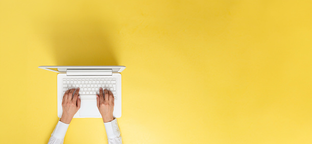 Unrecognizable person is working with laptop on yellow background.