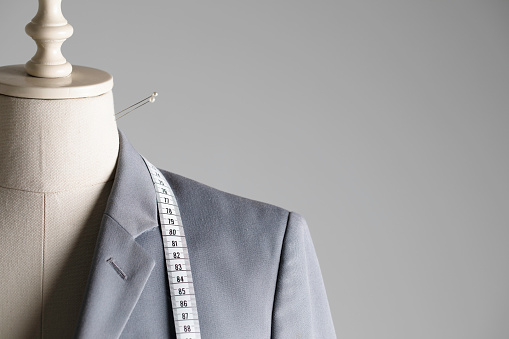 Tailor Mannequin with measure tape wearing gray suit in front of dark background.