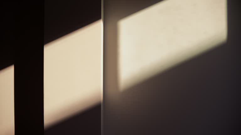 Bright sunlight and window shadow appearing on the wall in dark room and changing position until the room is getting dark again during sunset.