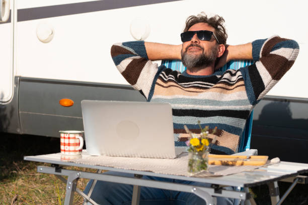 One man digital nomad lifestyle working on alternative outside workplace desk with a camper van motorhome house in background. People and office freedom. Modern small business concept job traveler stock photo
