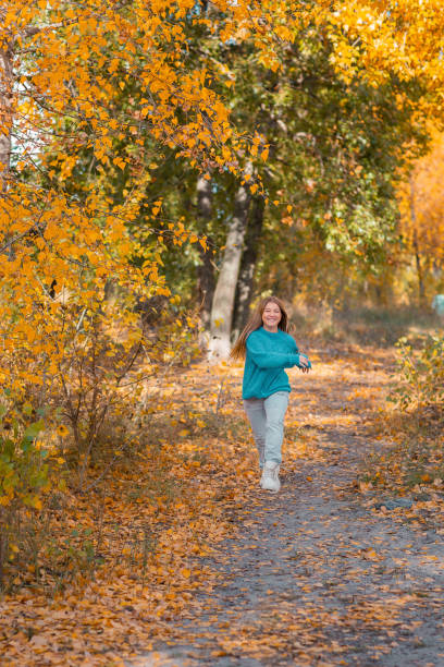 10대 소녀가 강 근처의 가을 공원을 혼자 걷고 있다. 그녀는 즐겁고 행복합니다. - wading stone cheerful happiness 뉴스 사진 이미지