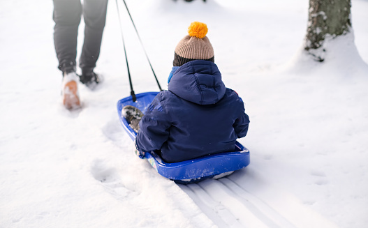 Dad takes his son on a sled through the snow in the park.
