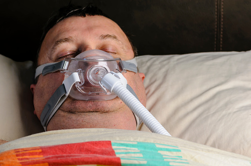 A middle-aged, overweight man wearing a CPAP mask while sleeping in bed