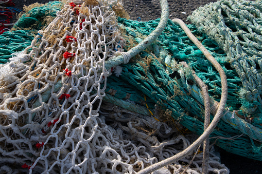 Fishing nets piled high at a commercial dock with the hull of two fishing boats in the background.  Port Andratx, Mallorca, Spain.