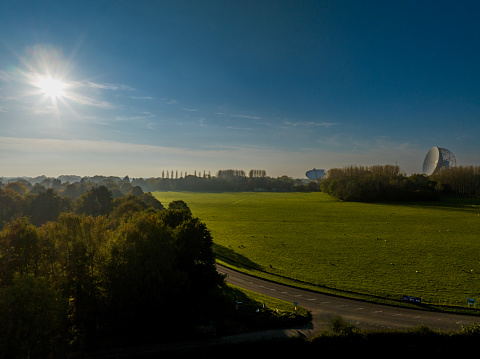 An aerial photograph of Jodrell Bank, Cheshire, England. The photograph was produced on a late autumn afternoon. The photograph shows autumnal trees on the left with the Jodrell Bank telescope on the right, pointing towards the sun