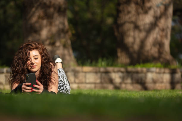 Pretty young lady is lying on the grass in public park.
