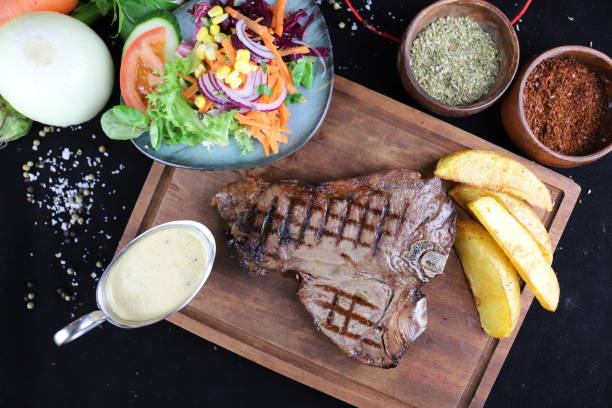 Grilled t-bone steak with salad and potatoes on wooden cutting board stock photo