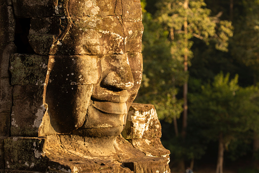 A huge face sculpted in stone, illuminated by the evening light at Bayon temple, Angkor, Cambodia.