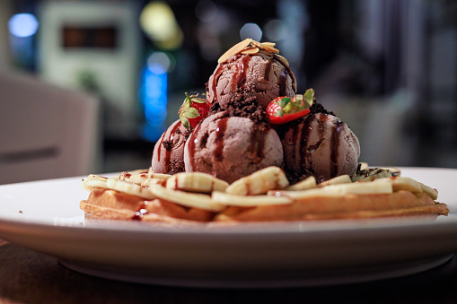 Belgian waffle dessert topped with chocolate ice cream, fresh strawberries and banana slices, and a decadent chocolate drizzle