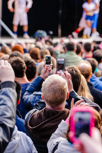 Belfast, Northern Ireland, UK.  06/06/2013 - Many people in the audience at an outdoor music concert at Belfast City Hall using mobile phones to take photographs and videos of the performance rather than watch the concert directly.  The concert was to welcome the arrival of the Olympic flame to Belfast, and the concert included many local bands including General Fiasco, Foy Vance and Snow Patrol.