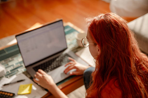 istock Red-haired girl with glasses, using a calculator and paying bills online - Multitasking 1763102067