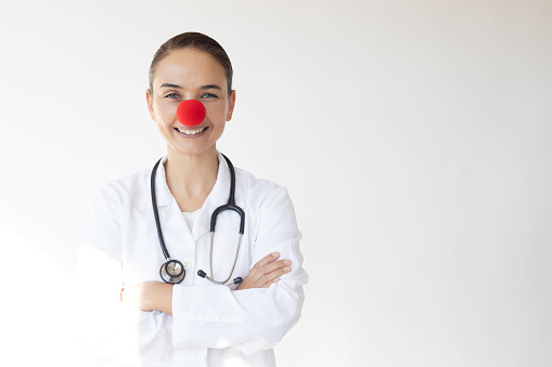 Doctor with red clown nose and with a toothy smile in front of white background.