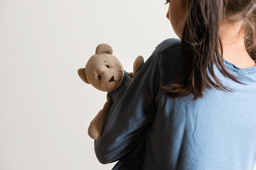 Back view of little caucasian girl who is hugging her teddy bear in fear. Representing child abuse and domestic violence.