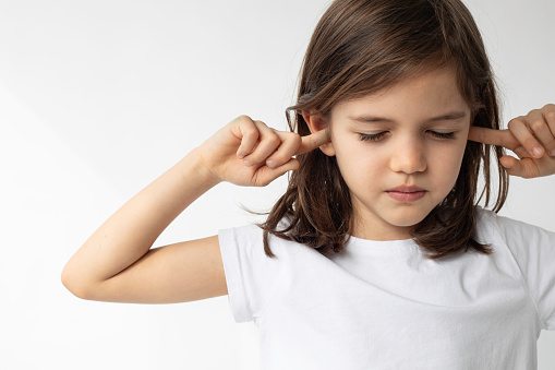 Little girl covering her ears with fingers isolated on white background.