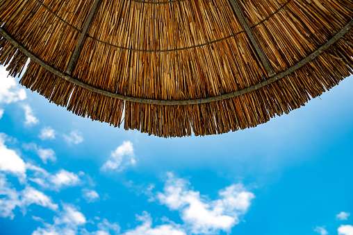 Sky with clouds under straw bamboo umbrella.