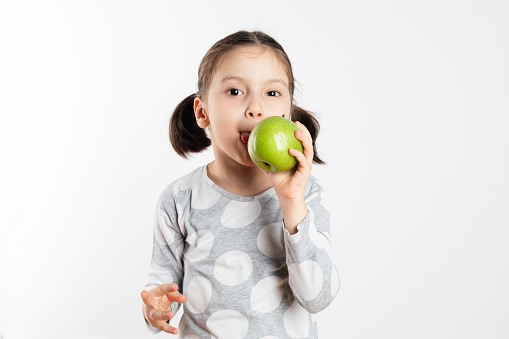 Little girl is about to eat a green apple and is looking at camera .