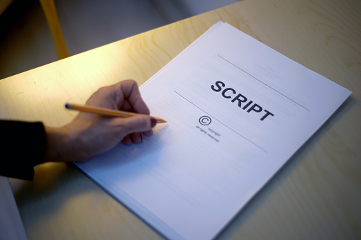 script papers for filming movie making notes with pencil. Woman edits text at wooden table in office and prepares for playing role