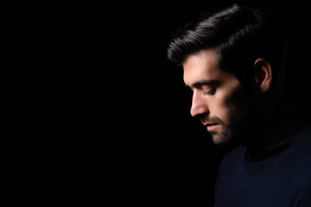 istock Bearded man bend down the head in dark room Guy looks down on black background with side view Concept serious depression and dismal Alone businessman close eyes and hopeless depressed He get lonely 1763263367