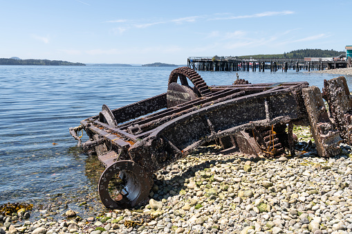 Abandoned Machinery  on the beach of Alert Bay with an old disused pier behind behind, British Columbia, Canada
