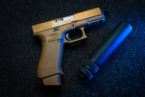 istock Sand colored pistol and silencer on the black desk illuminated from the side, side view 1763301474