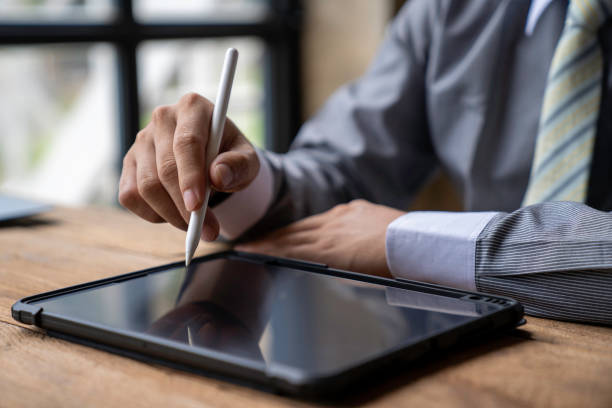 istock Man working contemporary electronic tablet while sitting at the wooden table at office.Men using digital stylus for pointing device screen.Blurred background. Horizontal 1763309416