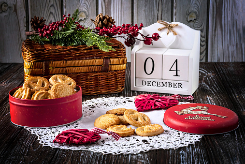 Cookies in a red box and a calendar on the table. Concept for National Cookie Day, December 4. Christmas tree and toys as decor on a wooden background.