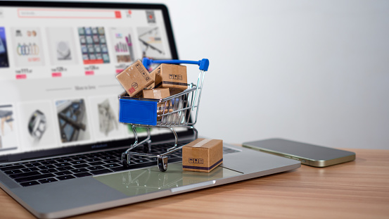 Shopping cart and product boxes placed on laptop computer represent online shopping concept, website, e-commerce, marketplace platform, technology, transportation, logistics and online payment concept.