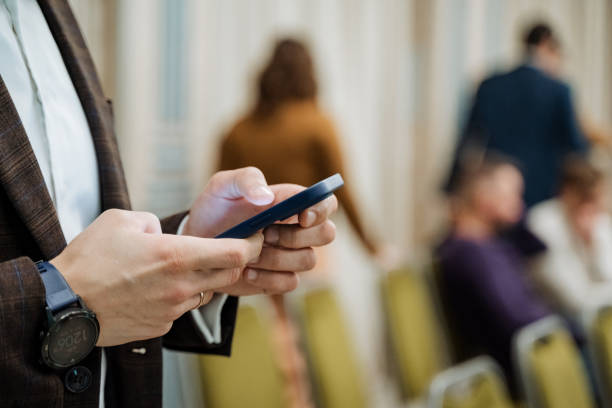 A businessman prints a message on his phone during a conference. A smartphone in the hands of a young guy. Write text with your fingers. Watch on hand.