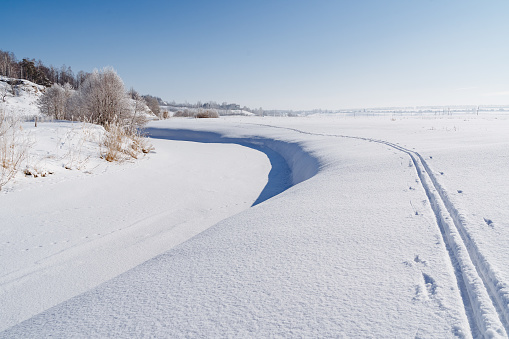 Ski tracks pass next to the frozen riverbed. Winter beautiful landscape. Large snowdrifts, a ski trip in the park. High quality photo