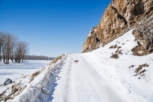 The road is covered with snow over the horizon against the background of a blue sky. Winter road in the mountains. Clear weather. High quality photo