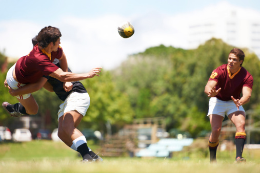 A rugby game caught mid action with a rugby player being tackled and passing the ball to his team member
