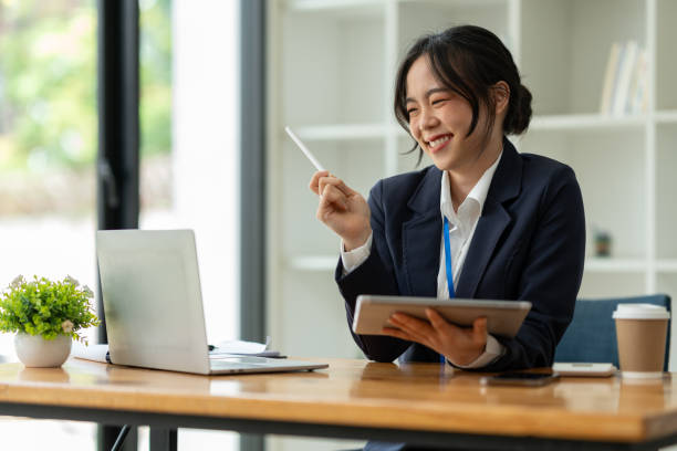 smiling asian business woman delight in the achievements by using the tablet to work with plans, ideas, ideas to present. financial report business plan investment new age concept online - news of the world imagens e fotografias de stock