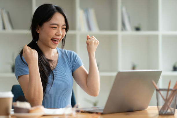 istock Asian woman sitting at work happily, smiling, delighted with business success feedback data from smartphone and data on laptop. while sitting on a desk in his office at home 1763347202