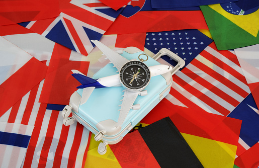 Compass, airplane and suitcase on  national flags background. Choosing travel direction concept.