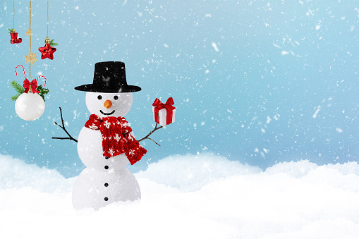 Snowman with Christmas present over blue background with copy space. Merry Christmas and Happy New Year greeting card. Winter holiday wallpaper.