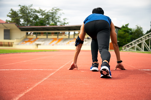 Portrait of strong willed athlete with prosthetic leg in start position on running track, looking confidently at camera