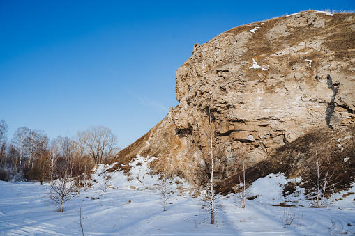The sun illuminates a large rock, a mountain against the background of a blue sky, a landscape of Natural Nature of Russia, the southern Urals of Bashkortostan, the Karlamanskaya Cave