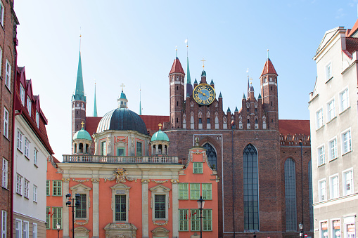 View of the old Catholic church with towers, ancient clock, with domes, orange walls and dark brick walls, and with tall windows. Gothic religious architecture. Poland, Gdansk, April 2023