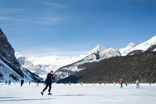 Lake Louise, Alberta, Canada - March 17, 2023: Tourists ice skate on the frozen lake in Banff National Park in front of the Fairmont Chateau hotel.