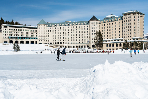 Lake Louise, Alberta, Canada - March 17, 2023: Tourists in ice skates play hockey on the frozen lake in Banff National Park in front of the Fairmont Chateau hotel.