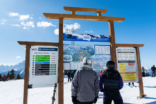 Lake Louise, Alberta, Canada - March 20, 2023: People study the ski run map to decide which trail to take down the mountain on a winter day at Lake Louise Ski resort in Banff National Park.