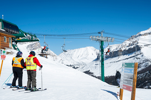 Lake Louise, Alberta, Canada - March 20, 2023: A blind man skis down a mountain wearing a vest to warn others of his disability and listens to verbal cues from his visiual guide who accompanies him at Lake Louise Ski resort in Banff National Park.