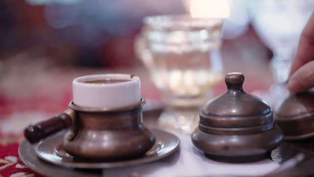 Close up of hand pouring traditional Turkish Coffee to small mug in café.