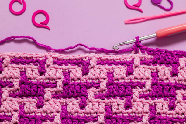 istock Crochet mosaic fabric close up with abstract pattern and crochet tools on a pink background. Copy space. 1763403738